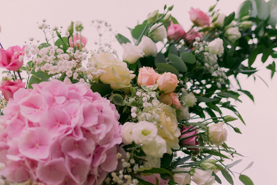 A close-up view of a floral arrangement featuring a variety of fresh flowers including large pink hydrangeas, creamy white roses, pale pink miniature roses, and sprigs of baby's breath, all arranged w