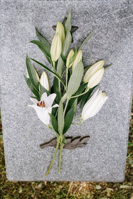 A bouquet of fresh white lilies with large, open petals and dark red stamens, arranged amidst long, green leaves. The flowers are displayed on a grey stone surface, with some lilies still in bud form 